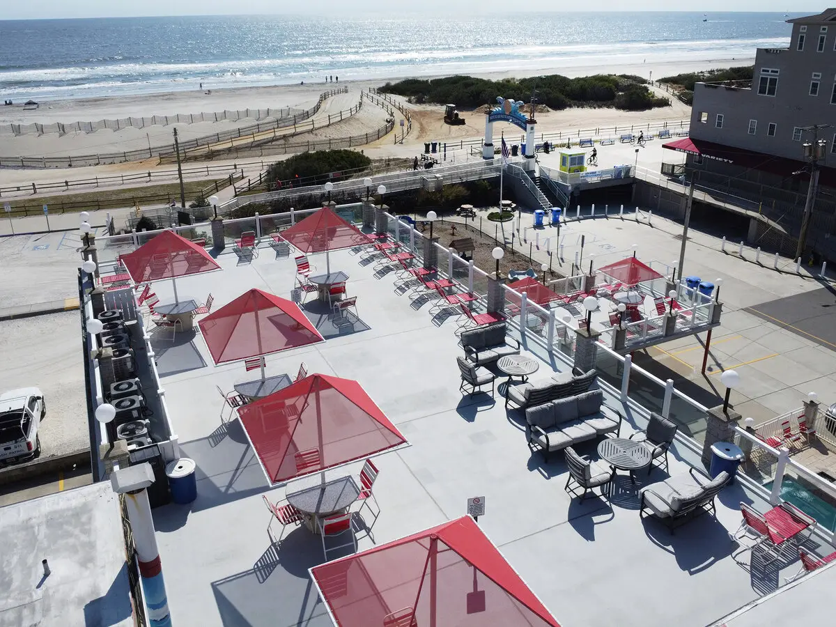 The Matador's oceanfront sundeck from above — red umbrellas and loungers, with the boardwalk, dunes and the Atlantic beyond