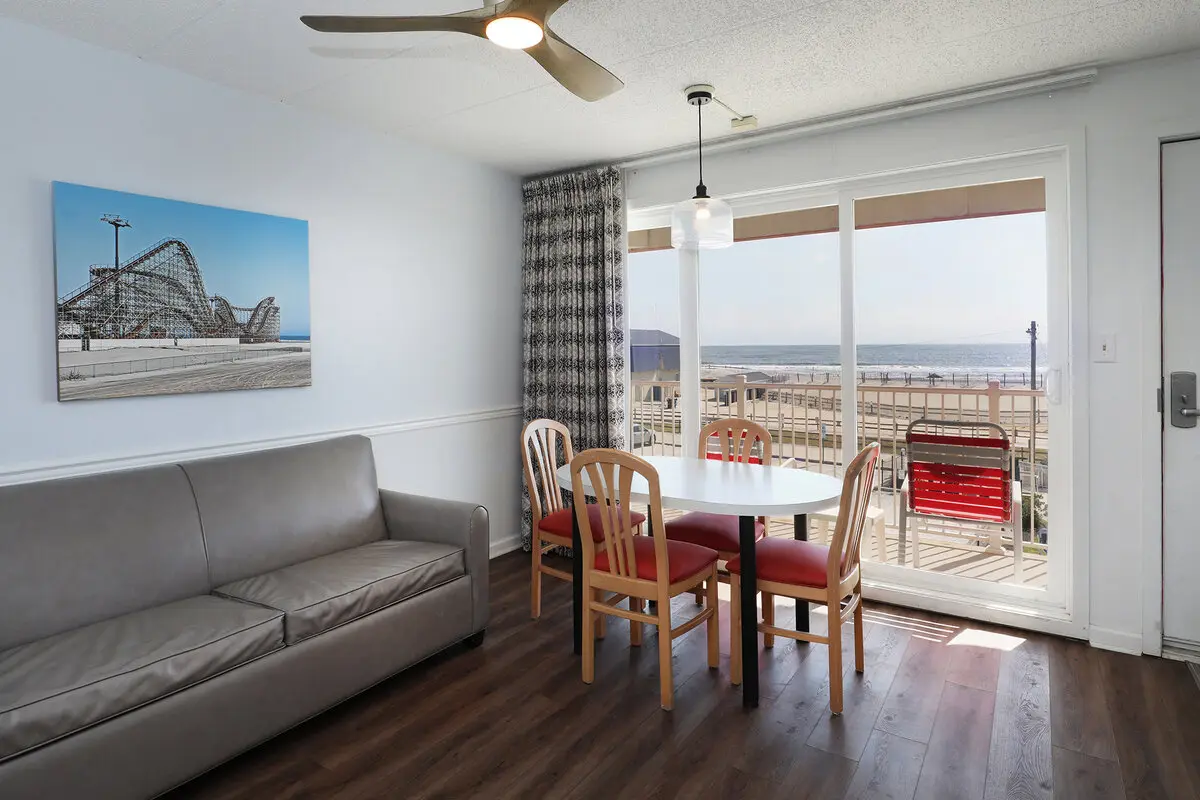 A living and dining area in an ocean-view unit at the Matador, with a sofa, a canvas print of the Wildwood rollercoaster and sliding doors onto a balcony overlooking the beach