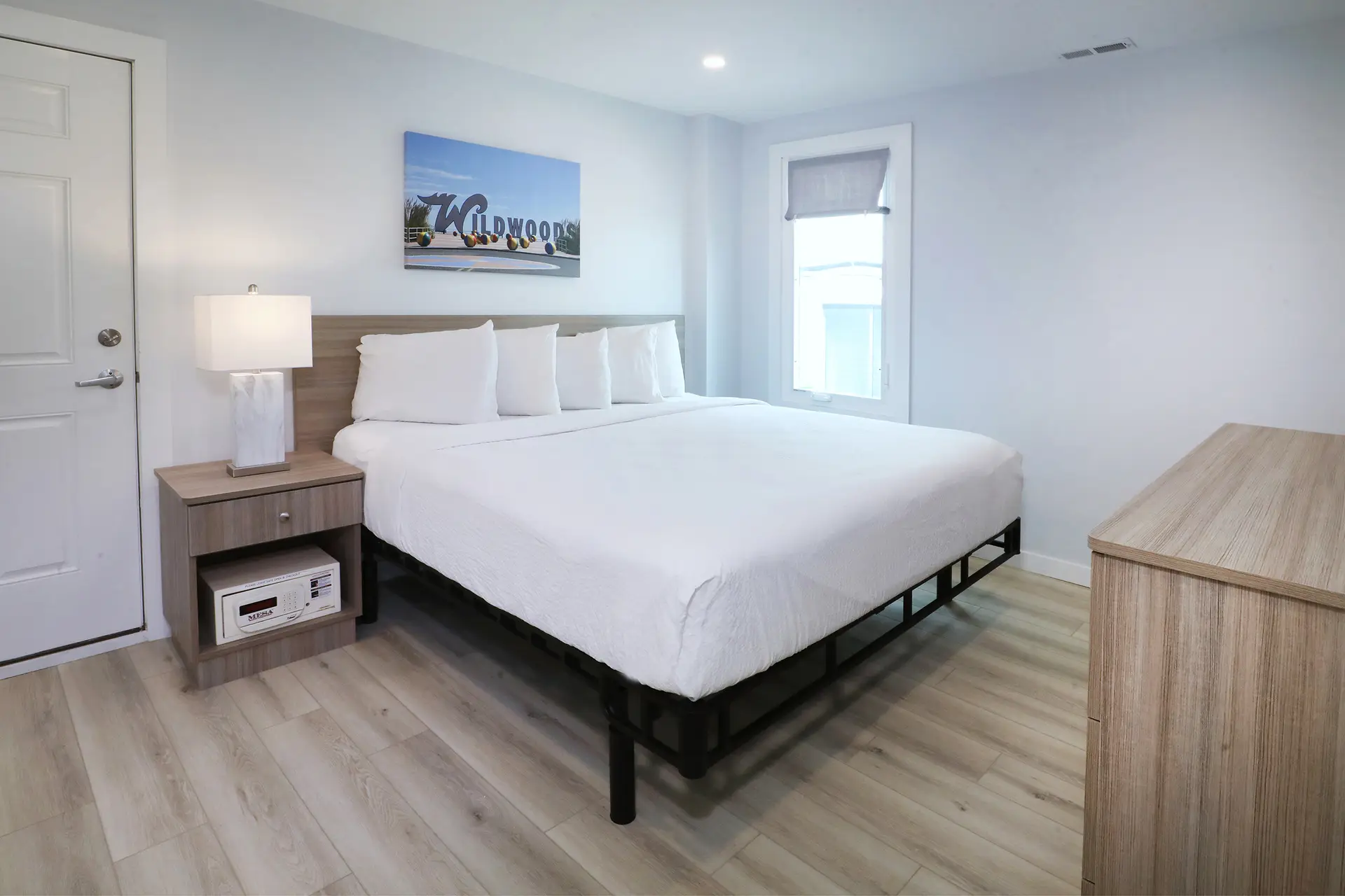 A renovated bedroom at the Matador with a king bed, in-room safe in the bedside cabinet and a canvas print of the Wildwoods sign