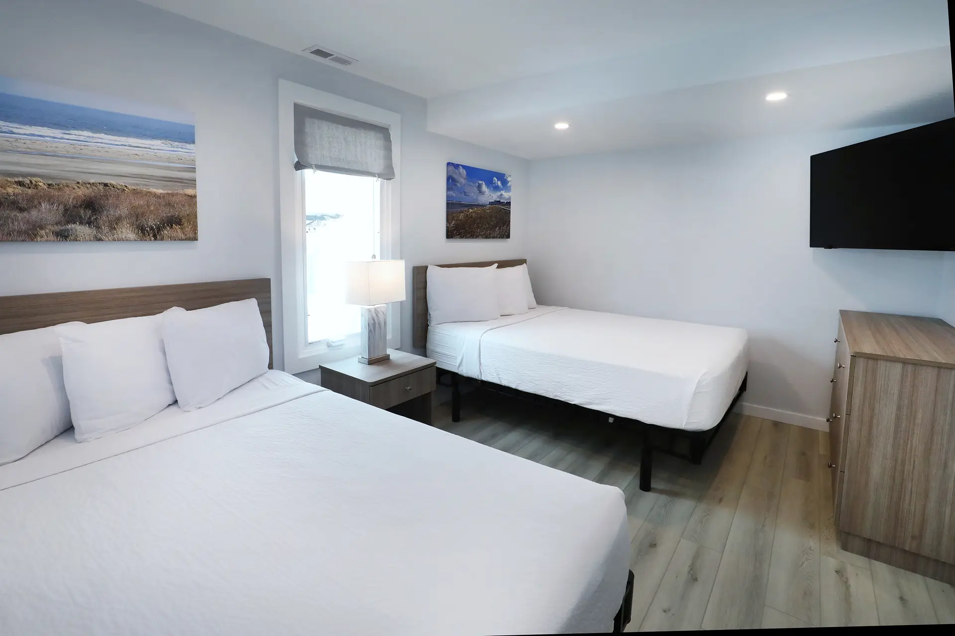 A renovated bedroom at the Matador with two queen beds, a wall-mounted television and framed photographs of the dunes
