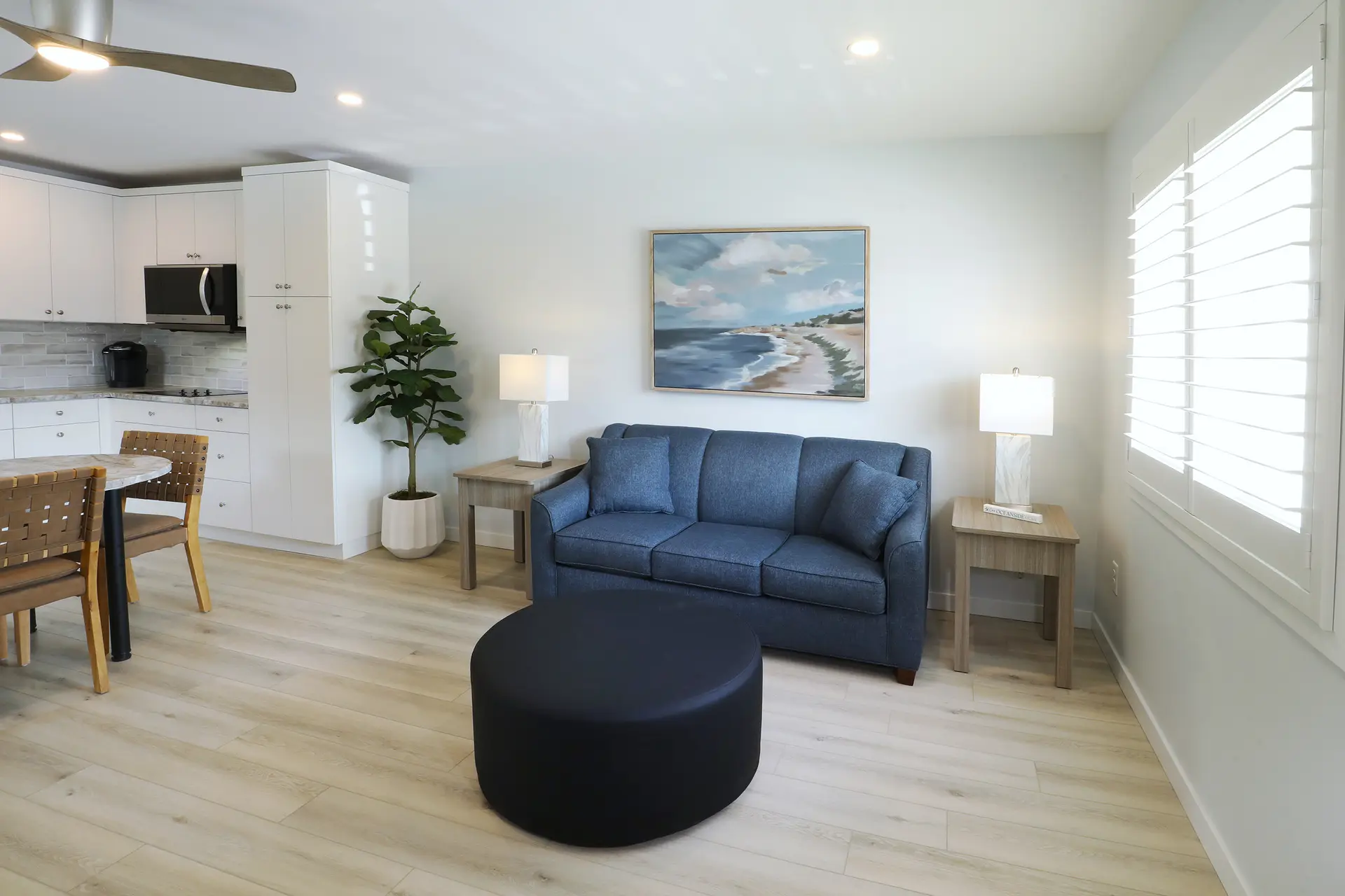 A renovated apartment at the Matador: open-plan living room with a blue sofa, ceiling fan and a white kitchen with a Keurig behind the dining table